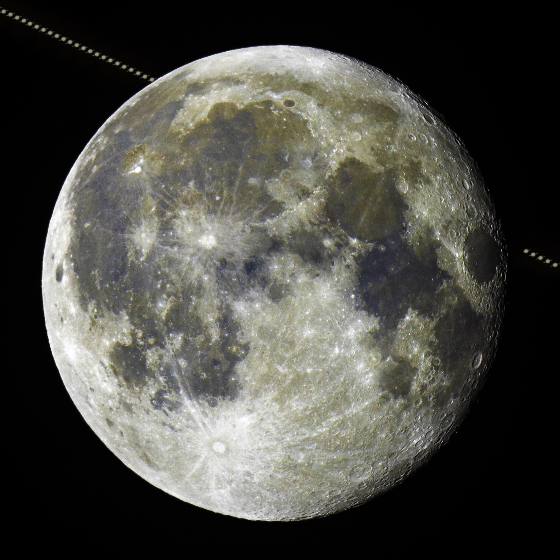 A photo of the full moon with a time-lapse of Saturn passing diagonally in the background.