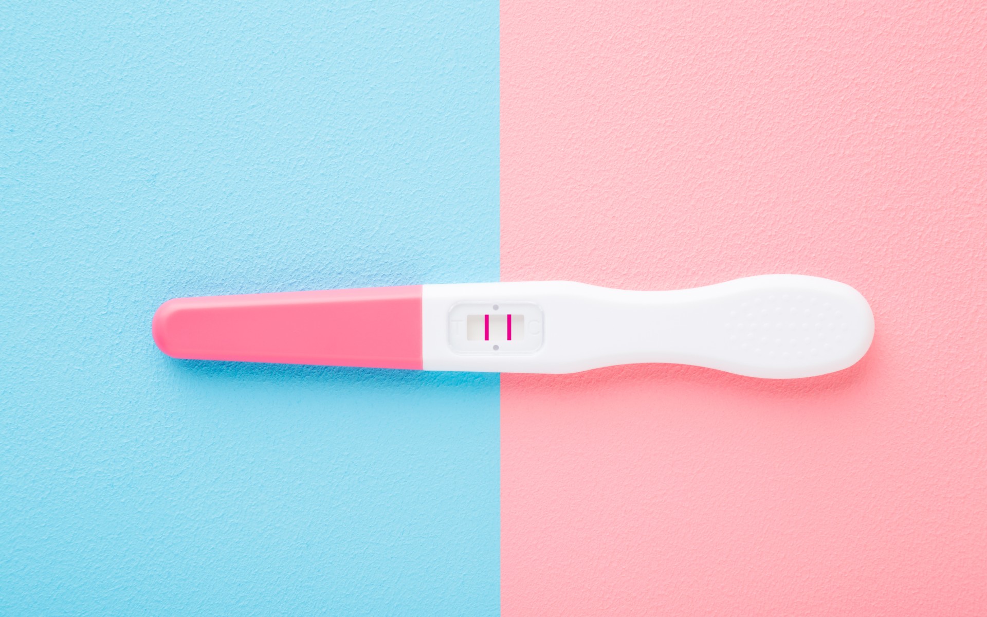 Pregnancy test with two stripes on light pink blue table background