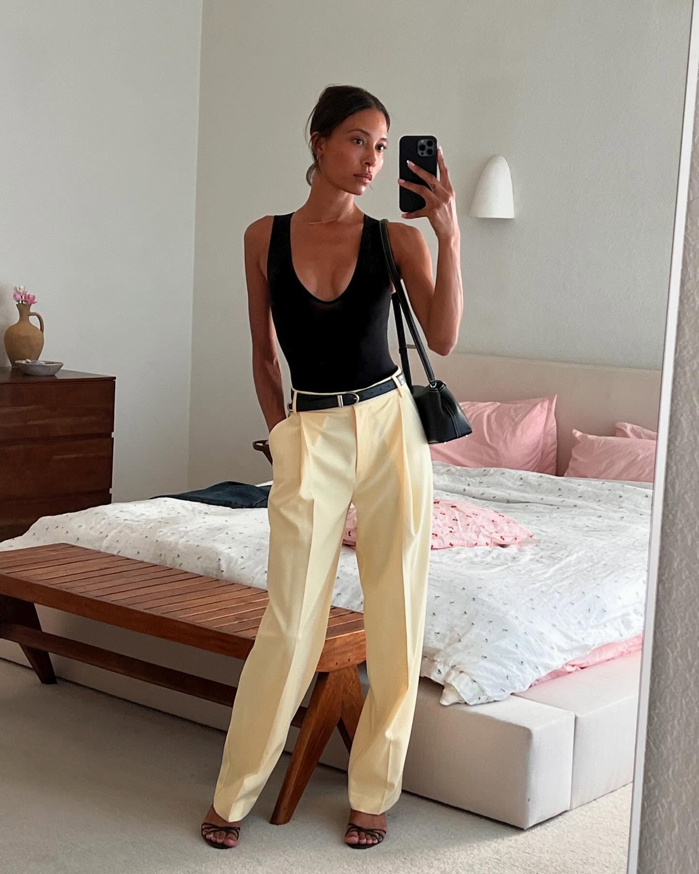 Tylynn wears a black tee, ivory trousers, and black strappy sandals.