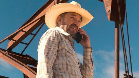 Tommy Norris talks on the phone in front of an oil rig