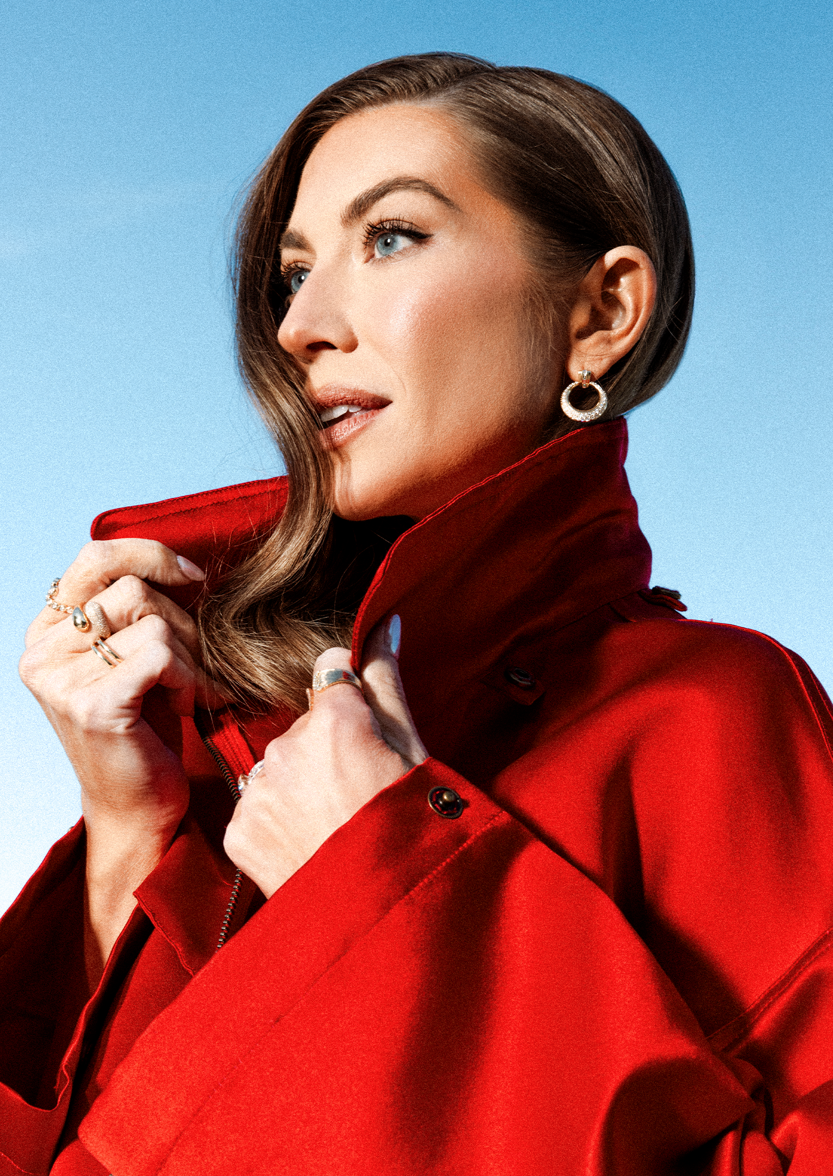 stassi schroeder wears a red trench coat with a tall neck, holding the collar as she poses in an editorial shoot