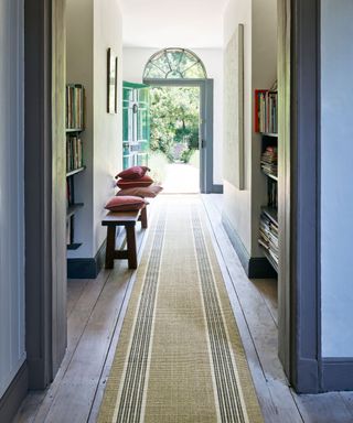 Traditional hallway with wooden floor, long patterned runner, looking out to open front door, wooden bench with cushions, shelves with books