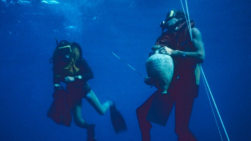 Two scuba divers holding artifacts while underwater