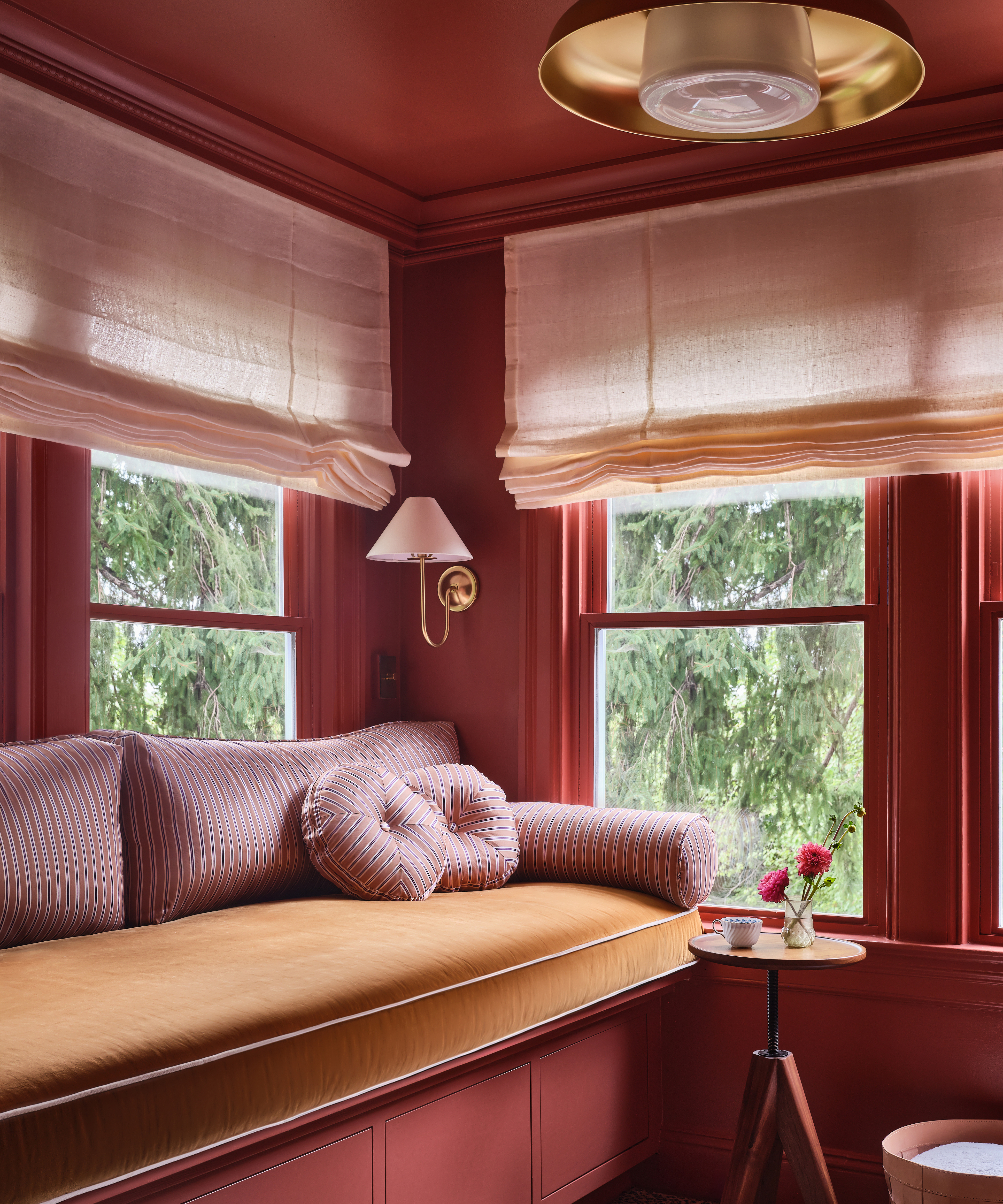 red room with large window seat in the corner and blinds on the windows