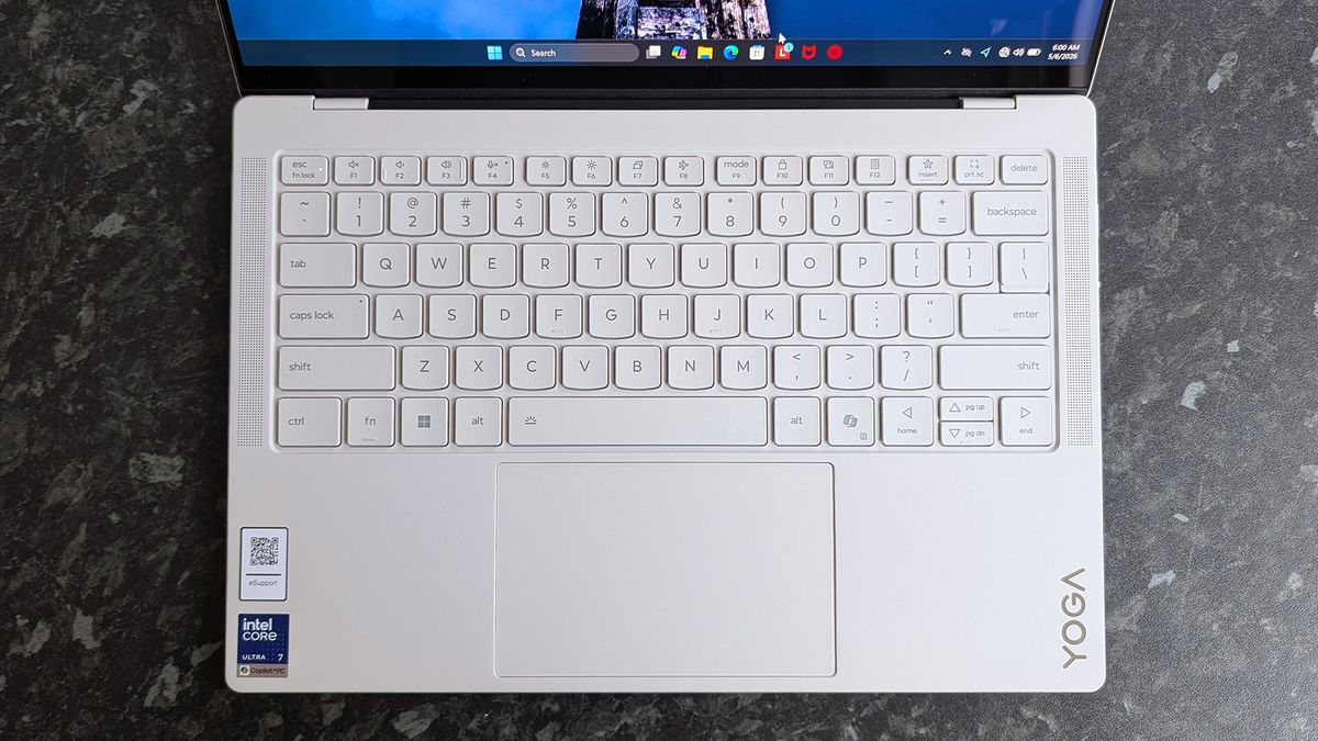 A Lenovo Yoga Slim 7i Ultra (Gen 11) Aura Edition laptop with a bright keyboard on a dark, textured surface. The brand name "Yoga" is visible beside the touchpad.