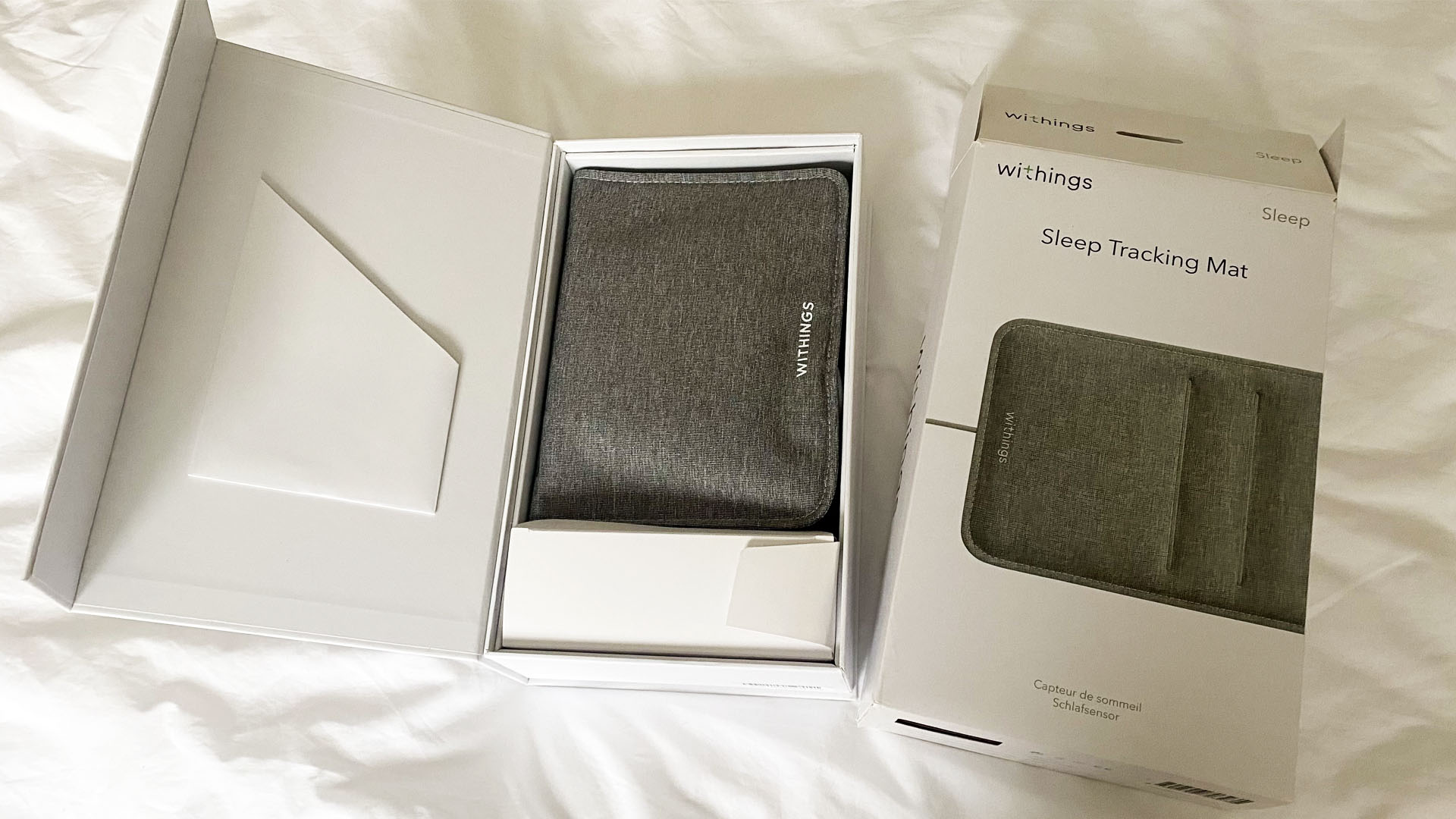 A Withings's Sleep Tracker Mat in its box (folded) on a bed in our reviewer's bedroom