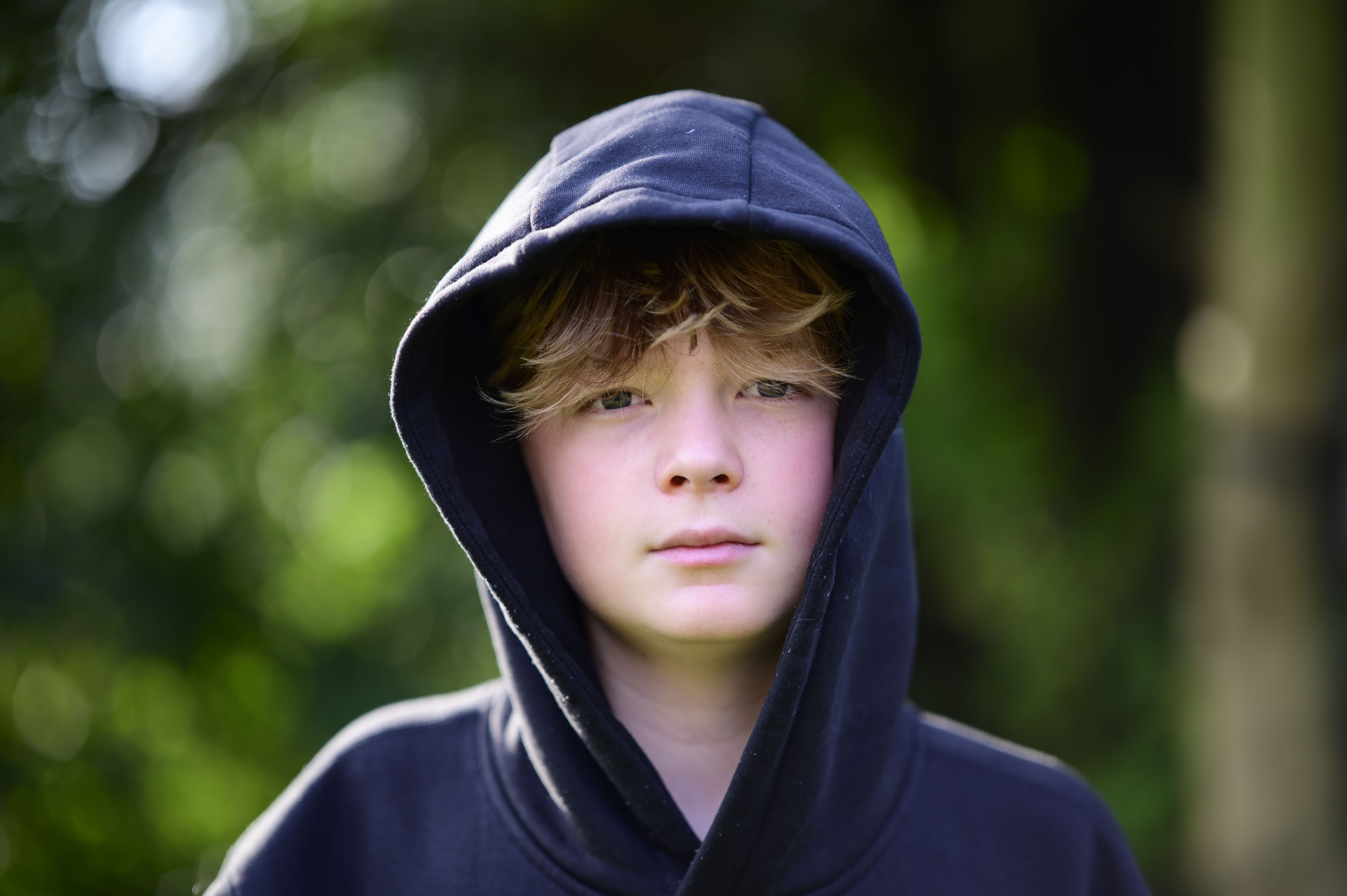 portrait of a boy in a hoodie with a dappled background light
