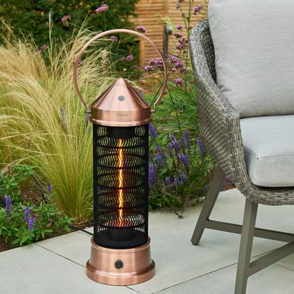 Kettler Kalos copper lantern patio heater on a paved patio by a grey wicker garden chair
