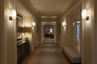 Basement hallway with striped runner, wood floor, neutral walls, wall lights and ceiling spots