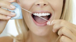 How to floss your teeth: image shows woman flossing teeth