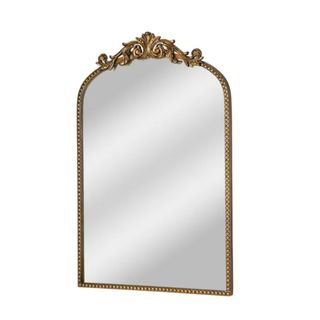 A curved brushed gold mirror with ornate detailing on the top and a silver reflection