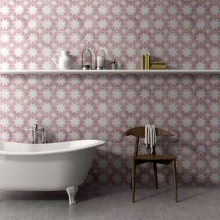 bathroom with pink and white star wall tiles, white freestanding clawfoot bathtub, long white wall shelf and brown chair next to bathtub