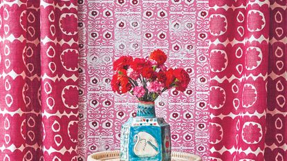 A vase of pink flowers against a hot pink curtained backdrop.