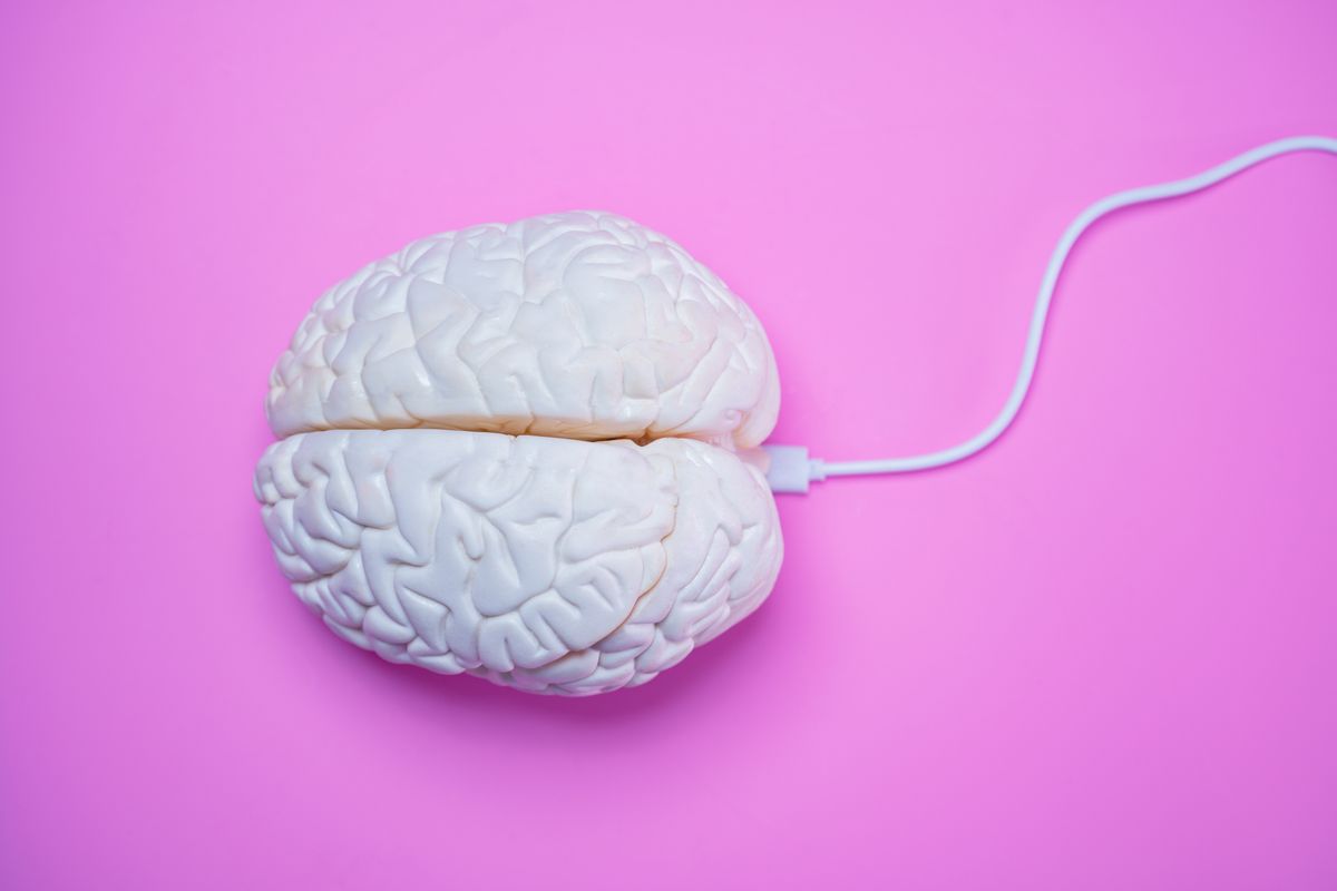 A brain connected with a cable, against a pink background