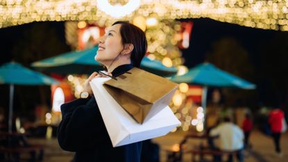 A woman holding shopping bags over her shoulder and looking up at Christmas lights 