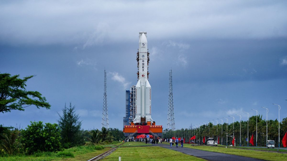 a white rocket upright on a launch tower surrounded by green, tropical trees