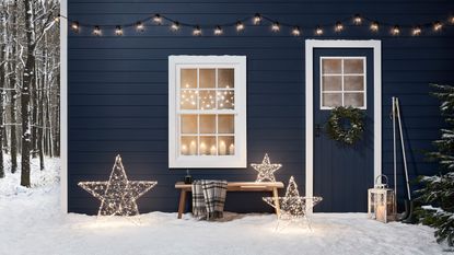 Outdoor Christmas decor at a cabin with three light up stars and fairy lights