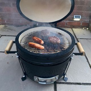 Kamado Maxi Ceramic Charcoal BBQ with cooked sausages and burgers on