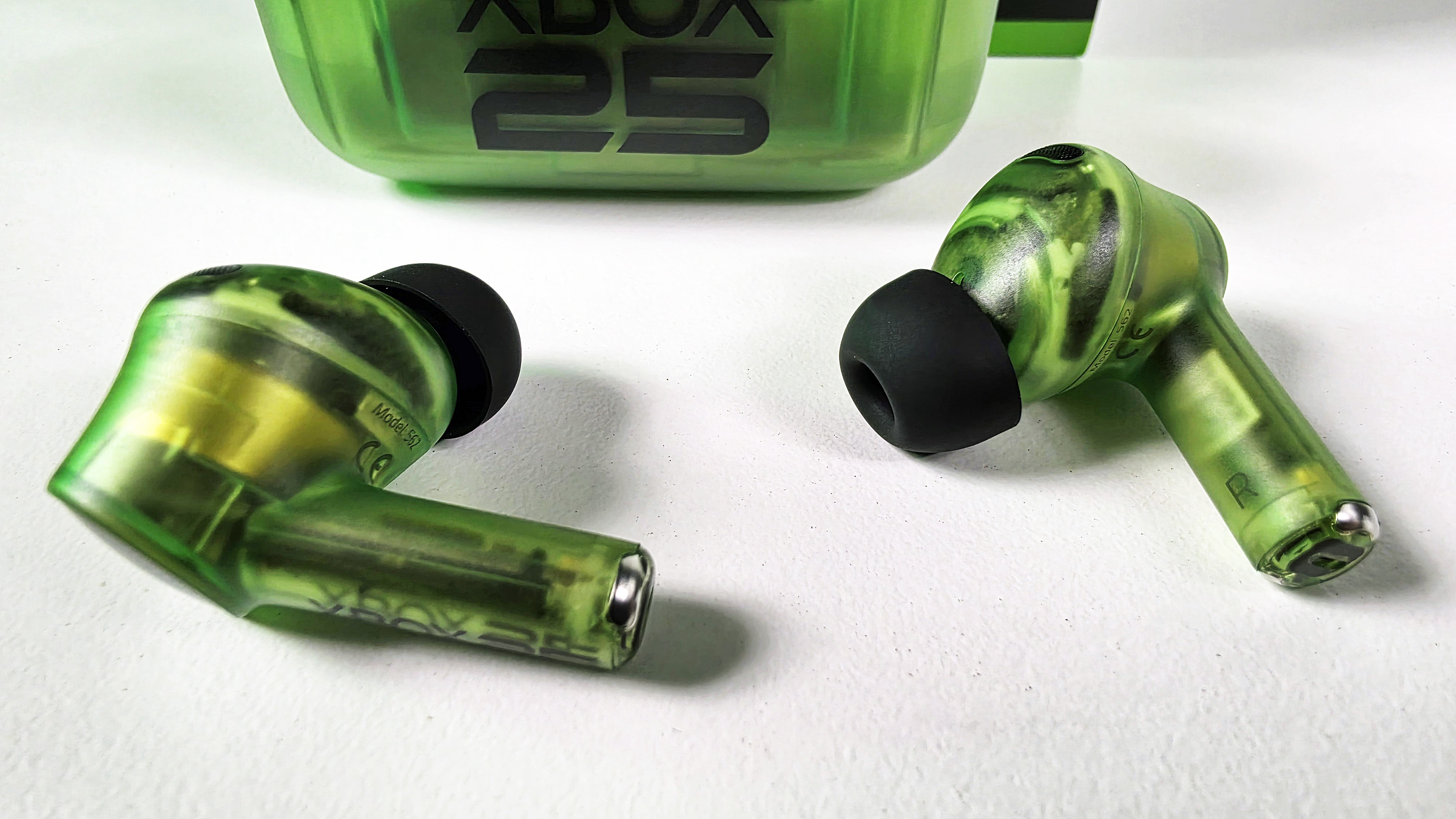 Close-up of the Razer Hammerhead V3 X HyperSpeed wireless earbuds in translucent green showing internal circuitry and black ear tips.
