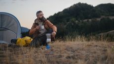 Man sitting in the wilderness outside his tent drinking a hot drink