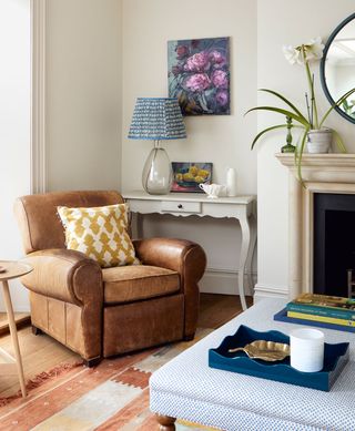 A brown leather armchair with yellow cushion, blue lamp and blue ottoman.