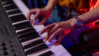 Close up of Musician Hands Playing Synthesizer Keyboard in Neon Lighting. Artist Producing Music in Home Studio, Recording Audio with Professional Equipment. Creative Arts and Hobby Concept.