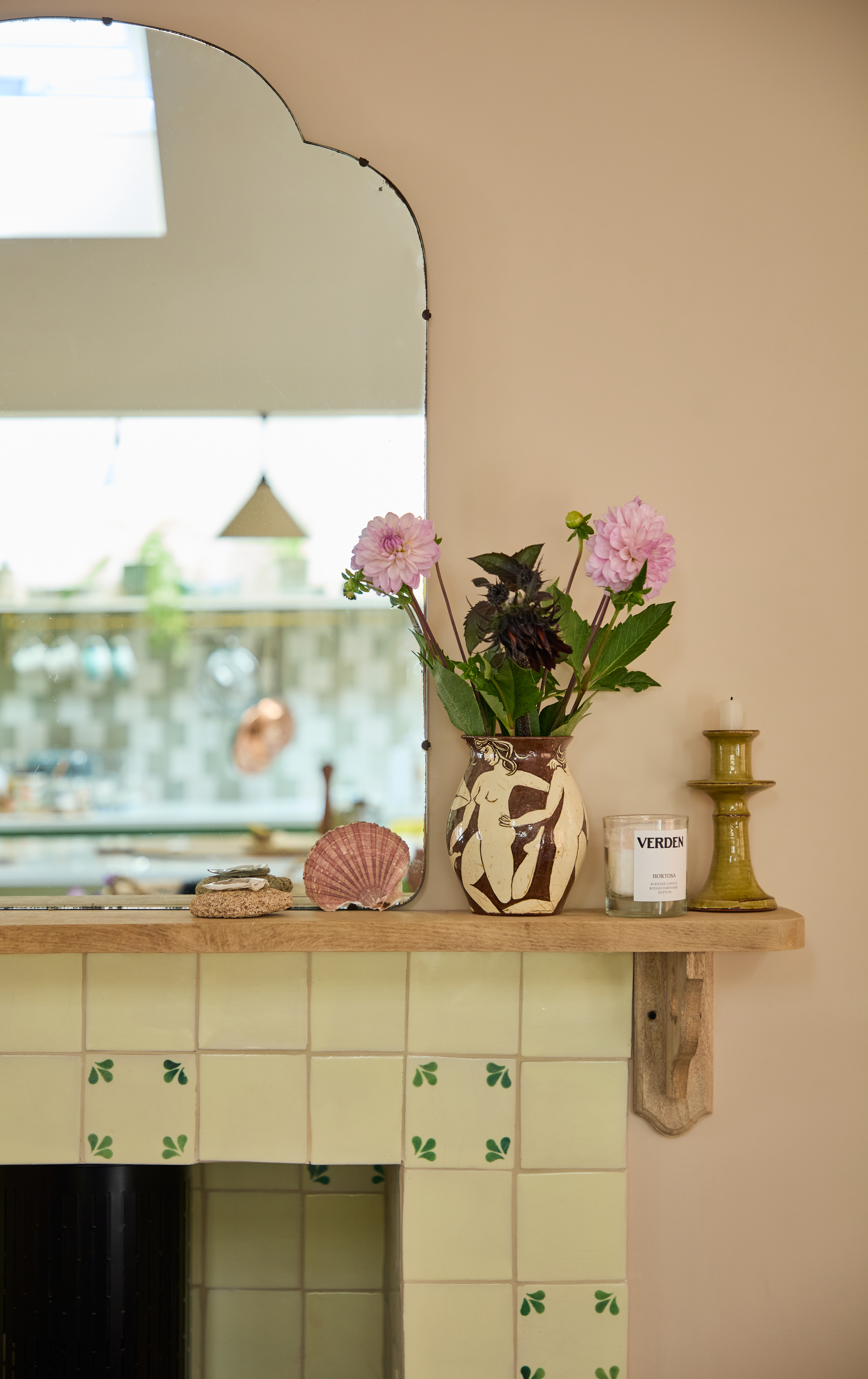 a fireplace mantel with a vase of dahlias and a candle