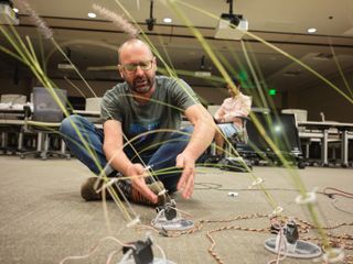 A man sitting on the floor working with devices connected to wheat figures.