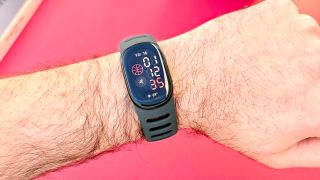 Close-up of the Fitbit Edge on a user's wrist against a bright red background