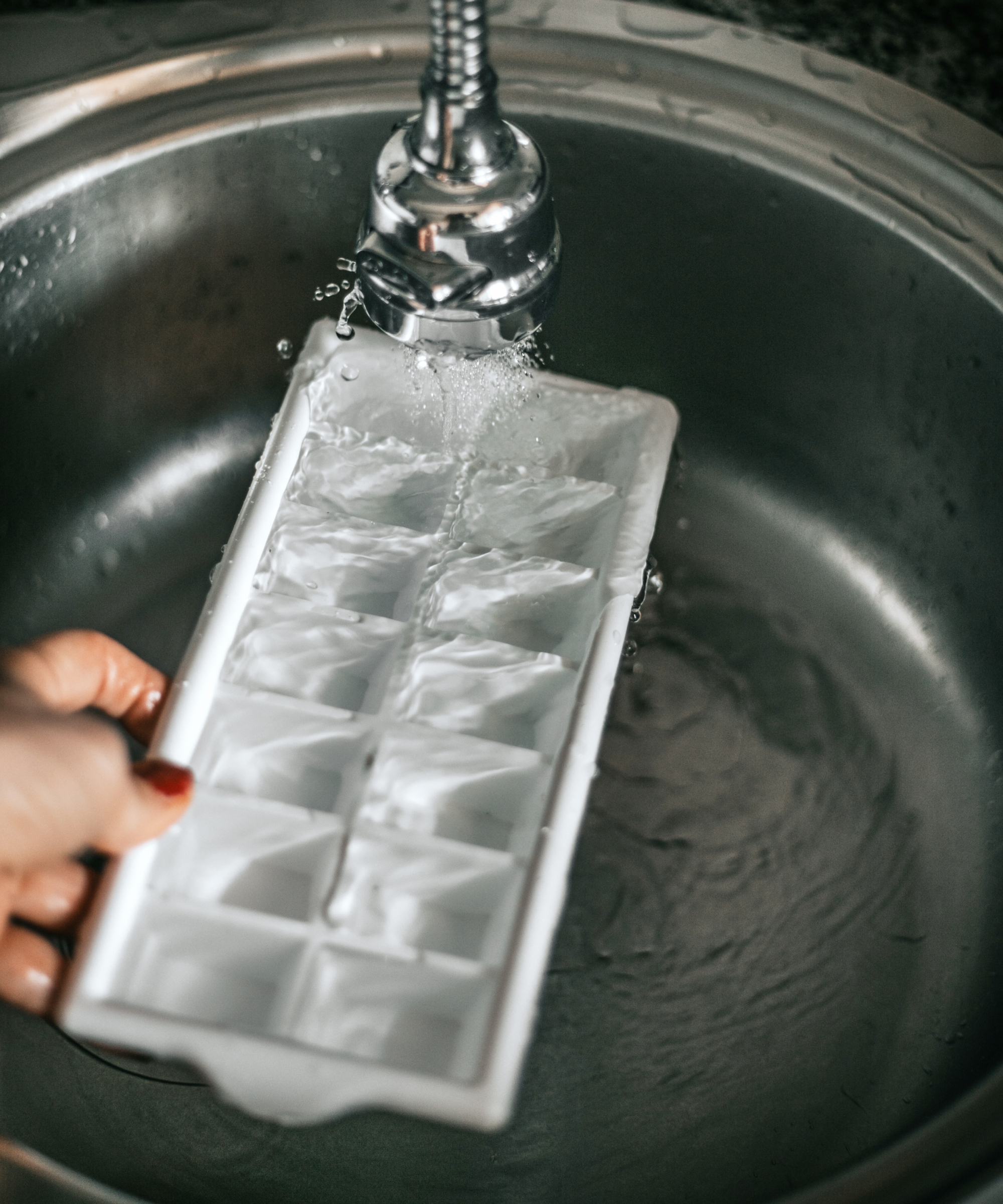 woman's hand filling ice cube tray under faucet