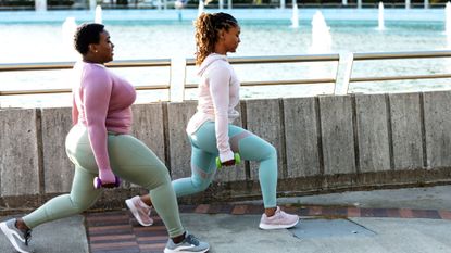 Two women performing dumbbell lunges outdoors