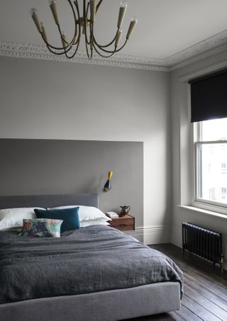 grey and white bedroom with two tone grey walls, dark wooden floor, dark grey abstract painted headboard, wall light
