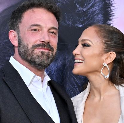 Ben Affleck wearing a black jacket and white shirt standing next to Jennifer Lopez who is looking at him and smiling 