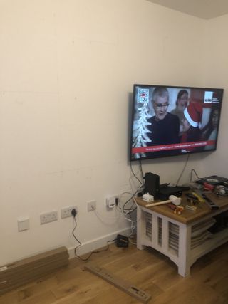 A living room with a small table in the corner and a TV mounted to the wall