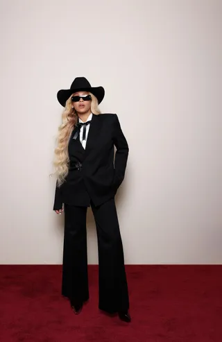 Beyonce wears a black suit and black cowboy hat in front of a plain wall