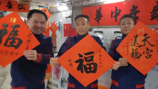 three astronauts holding red signs in a space station