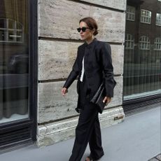 Influencer @deborabrosa wears a high-neck blazer with black straight-leg trousers and black strappy heels.