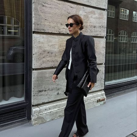 Influencer @deborabrosa wears a high-neck blazer with black straight-leg trousers and black strappy heels.