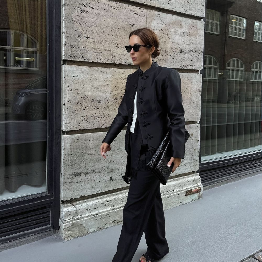 Influencer @deborabrosa wears a high-neck blazer with black straight-leg trousers and black strappy heels.