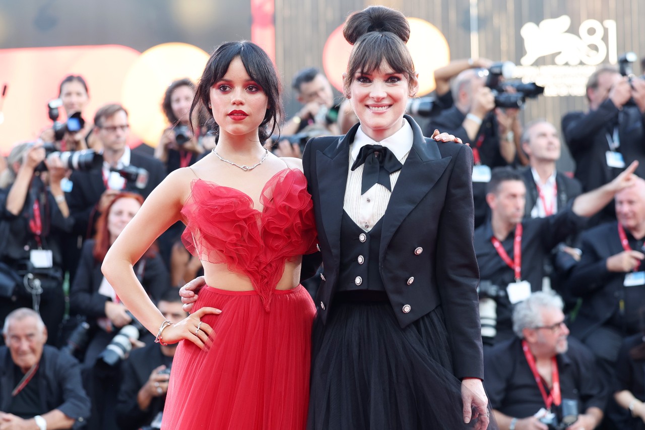 Jenna Ortega in a red dress and Winona Ryder in a black blazer and white button-down with a black skirt at the Beetlejuice premiere at the Venice International Film Festival on August 28.