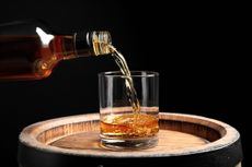 Pouring whiskey from bottle into glass on wooden barrel against black background