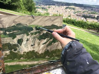 Artist's hand roughly applies blocks of green paint to the canvas