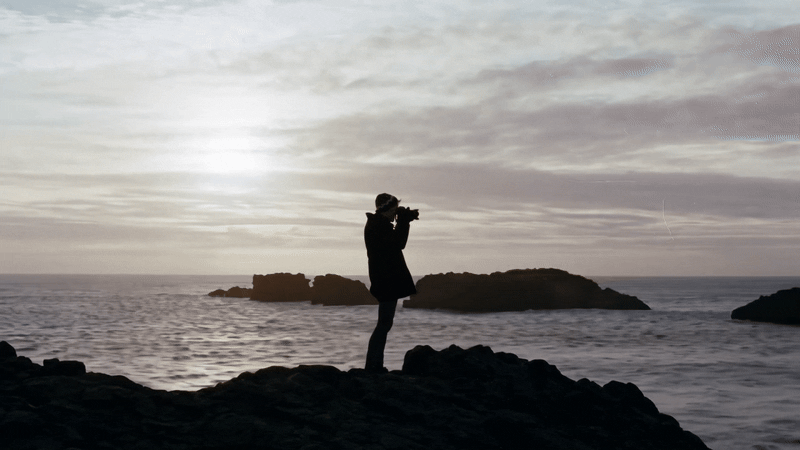 Motion gif of person standing on a cliff in front of the sea taking a photo