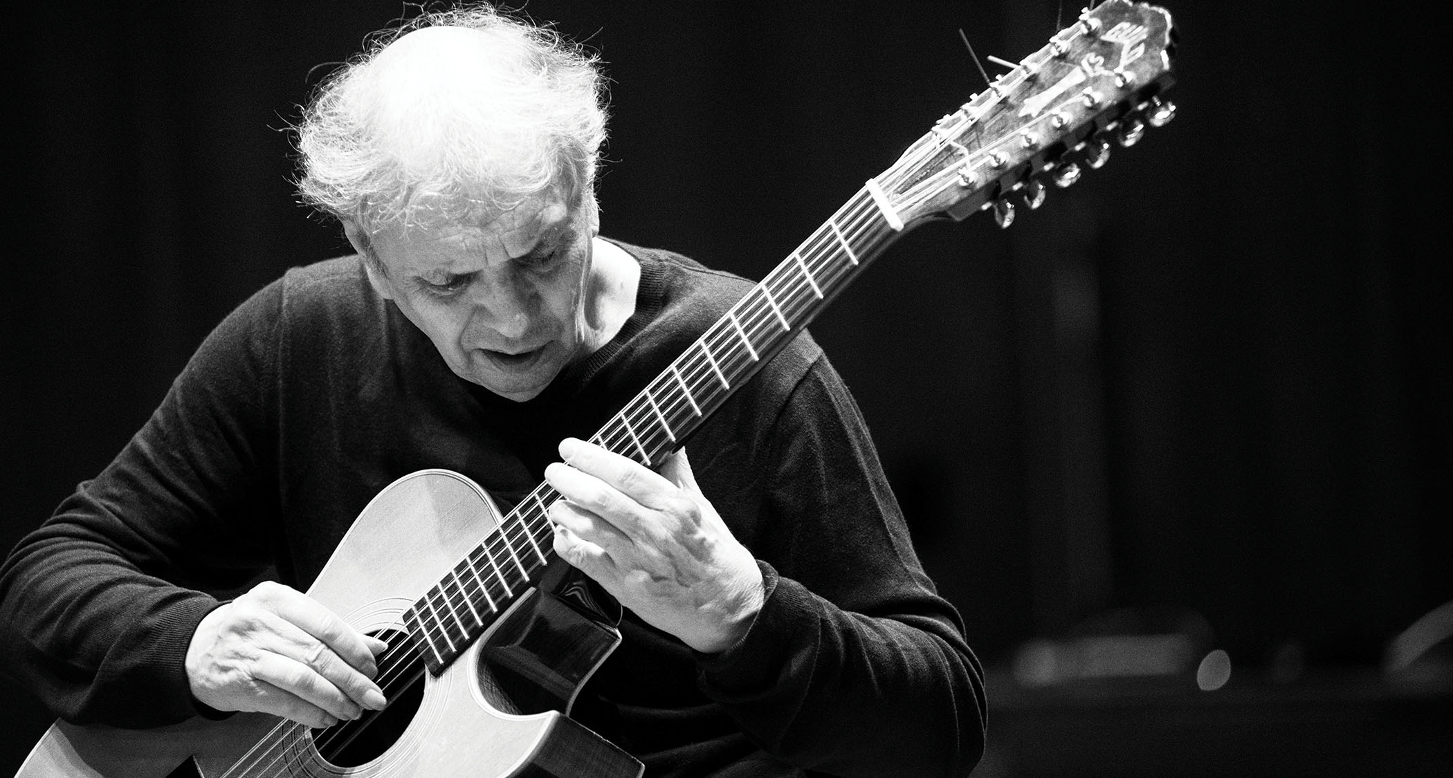A black-and-white portrait of Ralph Towner with his acoustic guitar