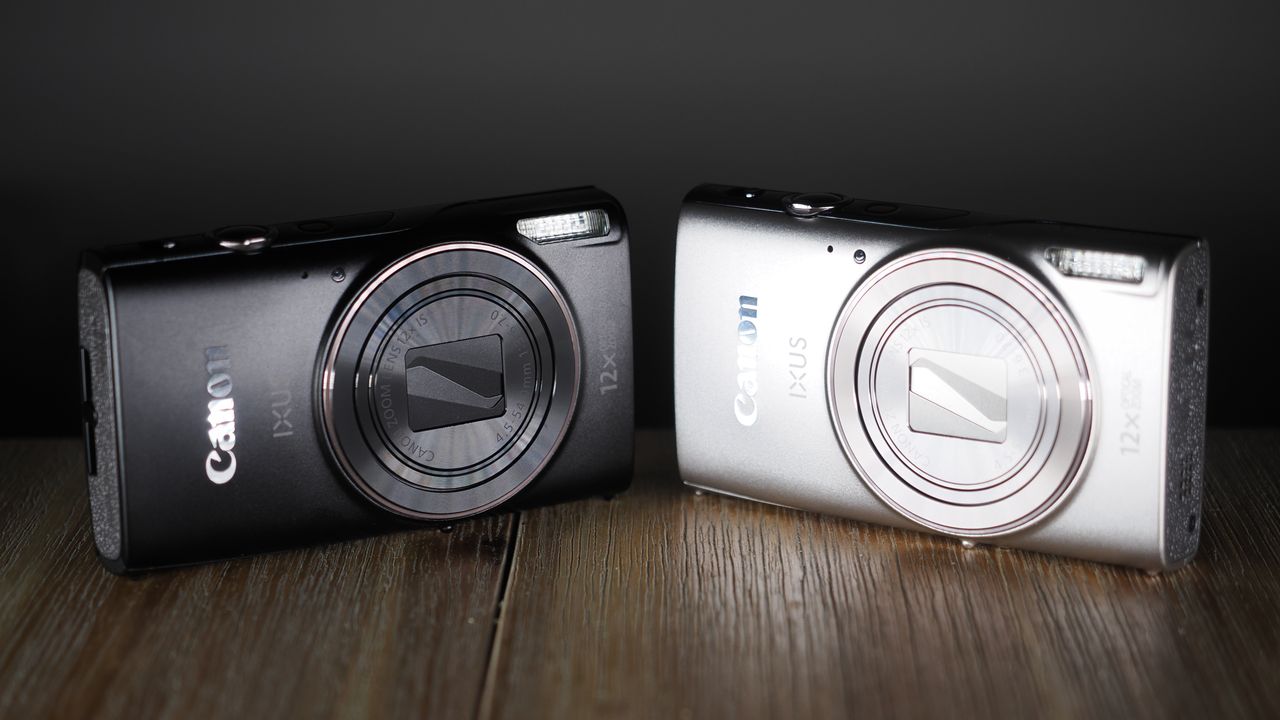 Canon Ixus 285 HS A in black and silver, side-by-side, on a wooden surface against a dark background