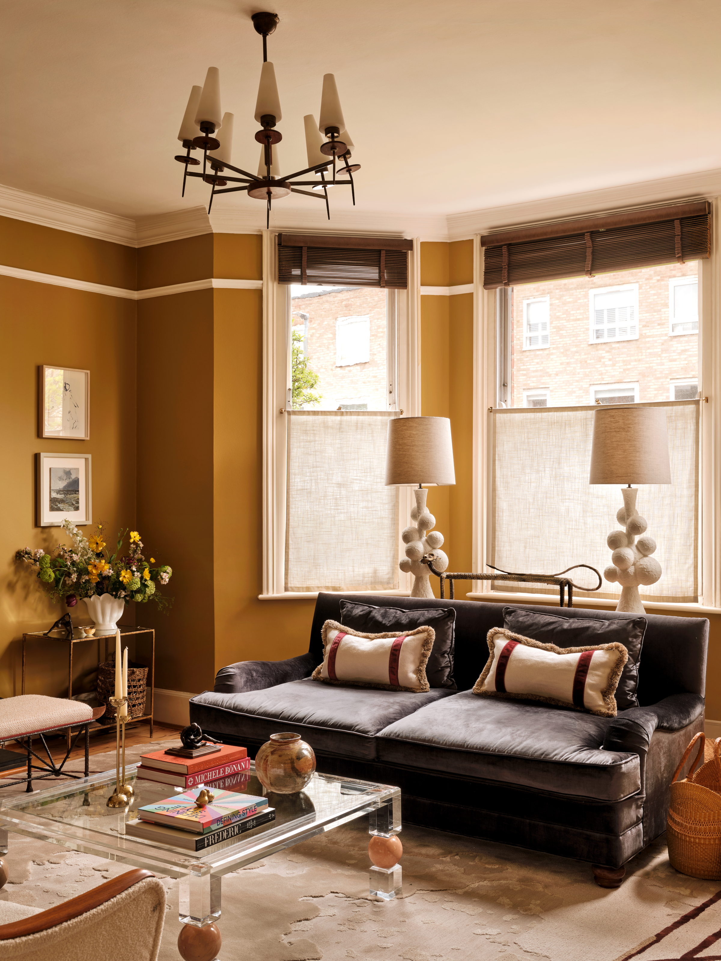 Living room with ochre painted walls, brown sofa, glass coffee table and cream floor lamps