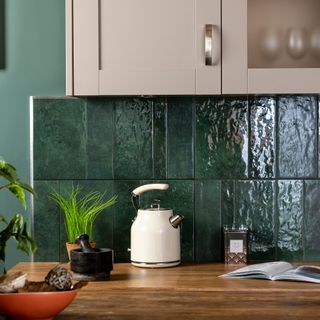 Dark green kitchen wall tiles with cream kettle in front.