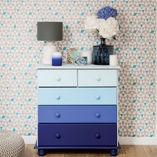 ombre effect drawers with wooden flooring and wallpaper on wall