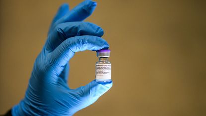 A covid vaccine held in surgically gloved hands