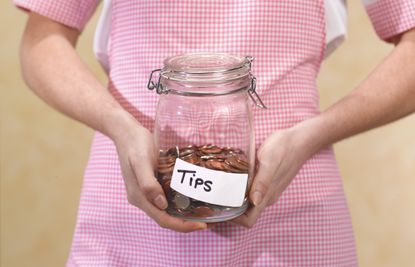 Waitress holding a jar full of coins that is labeled "Tips"